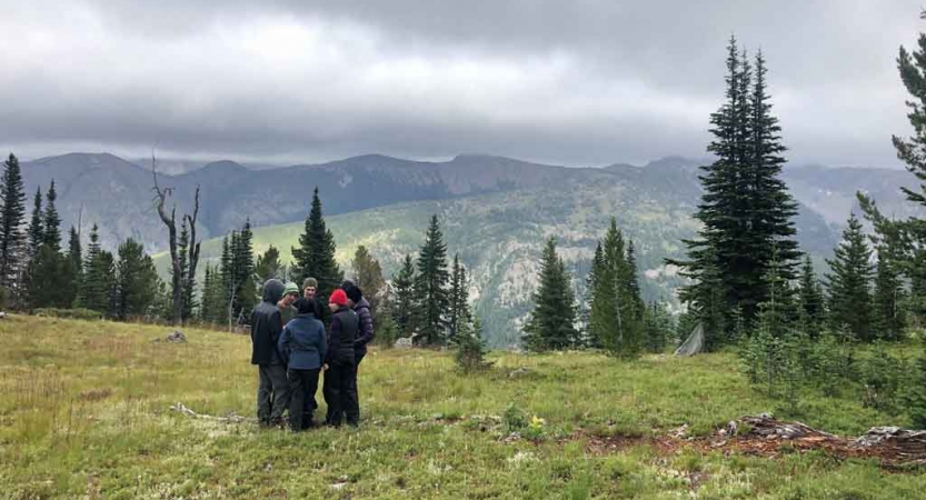 a group of students stand in a mountain meadow with a mountainous landscape in the background